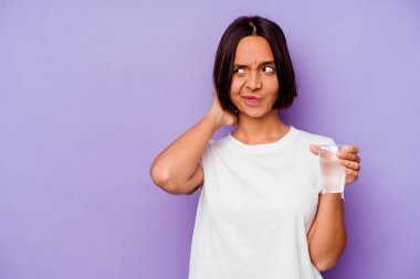 Mor arka planda izole edilmiş bir bardak su tutan genç melez ırk kafasının arkasına dokunuyor, düşünüyor ve bir seçim yapıyor..