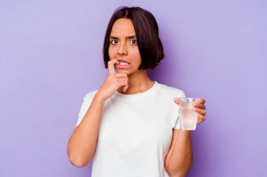 Mor arka planda izole edilmiş su bardağını tutan genç melez ırk tırnaklarını yiyor, gergin ve çok endişeli..