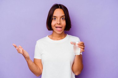 Mor arka planda bir bardak su tutan melez genç bir ırk hoş bir sürprizle karşılaşıyor, heyecanlı ve el kaldırıyor..