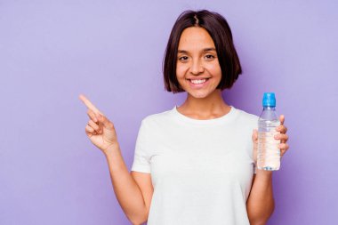 Mor arka planda izole edilmiş su şişesi tutan genç melez ırk gülümseyip boş alanda bir şey gösteriyor..