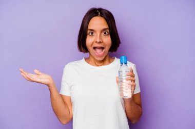 Mor arka planda izole edilmiş su şişesini tutan genç melez ırk şaşırdı ve şok oldu..