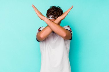 Mavi arka planda izole genç beyaz adam iki kolu çapraz tutuyor, inkar kavramı.