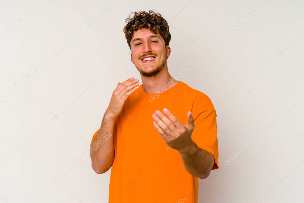 Young caucasian man isolated on white background pointing with finger at you as if inviting come closer.