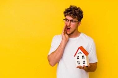 Sarı arka planda izole edilmiş bir model evi tutan genç beyaz adam gizli bir sıcak fren haberinin olduğunu söylüyor.