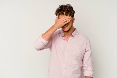 Beyaz arka planda soyutlanmış beyaz tenli genç bir adam elleriyle gözlerini kapatıyor, geniş bir gülümsemeyle bir sürpriz bekliyor..