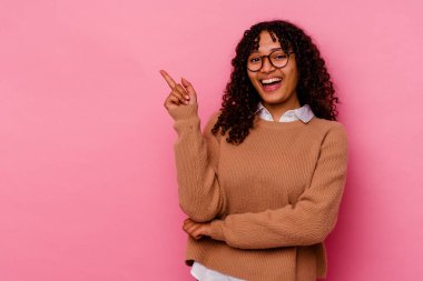 Pembe arka planda izole edilmiş genç melez kadın işaret parmağıyla işaret ederek gülümsüyor..