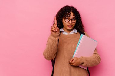 Genç öğrenci melez kadın pembe arka planda izole edilmiş. Bir numara parmağıyla görünüyor..