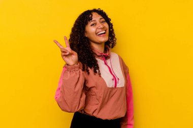 Genç melez kadın pembe arka planda izole edilmiş neşeli ve kaygısız parmakları olan bir barış sembolü gösteriyor..