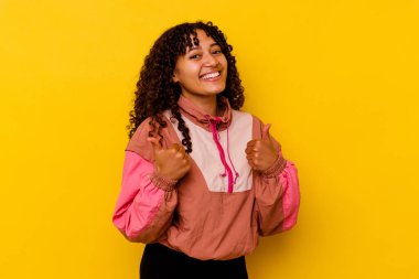 Pembe arka planda soyutlanmış genç melez bir kadın. Baş parmağını kaldırıyor, gülümsüyor ve kendinden emin..