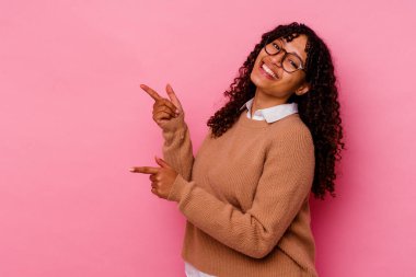 Pembe arka planda izole edilmiş genç melez bir kadın işaret parmağıyla işaret ederek heyecanlanıyor..