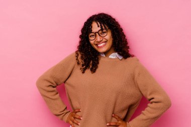 Pembe arka planda izole edilmiş genç melez kadın ellerini kalçasında tutuyor..