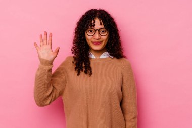 Pembe arka planda izole edilmiş genç melez kadın gülümseyerek beş numarayı parmaklarıyla gösteriyor..