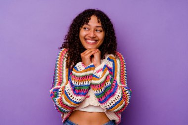 Mor arka planda izole edilmiş genç melez kadın ellerini çenesinin altında tutuyor, mutlu bir şekilde yana bakıyor..