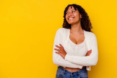 Sarı arka planda soyutlanmış genç melez bir kadın kollarını kavuşturarak gülümsüyor..