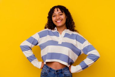 Sarı arka planda izole edilmiş genç, melez bir kadın ellerini kalçasında tutuyor..