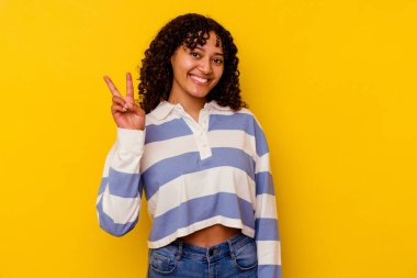 Sarı arka planda izole edilmiş genç melez kadın iki numarayı parmaklarıyla gösteriyor..