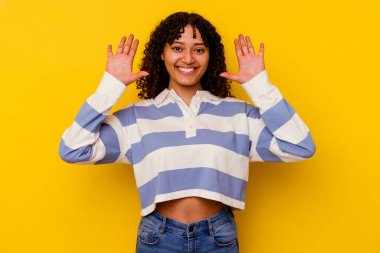 Sarı arka planda izole edilmiş genç melez kadın on numarayı elleriyle gösteriyor..