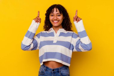 Sarı arka planda izole edilmiş genç melez kadın iki parmağı da boş bir alan gösteriyor..