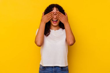 Sarı arka planda soyutlanmış genç bir ırk kadını. Gözleri ellerle kaplıyor. Gülümsüyor ve bir sürpriz bekliyor..