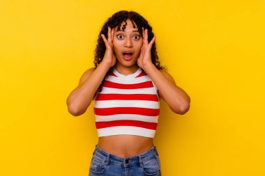 Sarı arka planda izole edilmiş genç melez kadın yüzünün yarısını palmiye ile kaplayarak eğleniyor..