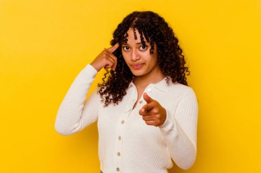 Sarı arka planda izole edilmiş genç melez bir kadın şakağı parmağıyla işaret ediyor, düşünüyor ve bir göreve odaklanıyor..