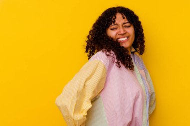 Sarı arka planda izole edilmiş, sırt ağrısı çeken genç bir ırk kadını..