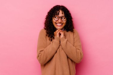 Pembe arka planda soyutlanmış genç melez kadın ellerini çenesinin altında tutuyor, mutlu bir şekilde yana bakıyor..