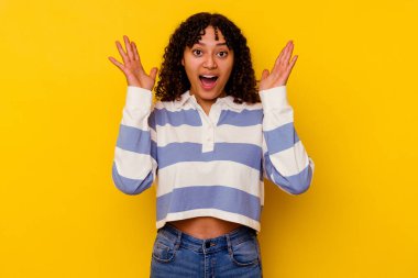 Sarı arka planda izole edilmiş genç melez bir kadın zaferi ya da başarıyı kutluyor, şaşırıyor ve şok oluyor..