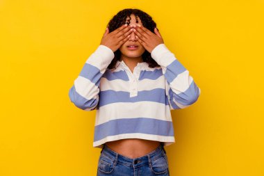 Sarı arka planda izole edilmiş genç melez kadın elleriyle gözlerini kapatmaktan korkuyor..