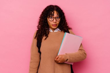 Genç öğrenci melez kadın pembe arka planda izole edilmiş omuz silkiyor ve gözleri açık..