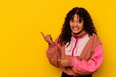 Pembe arka planda izole edilmiş genç melez kadın işaret parmağıyla fotokopi alanını işaret ederek şok oldu..