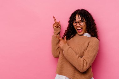 Pembe arka planda izole edilmiş genç melez kadın işaret parmağıyla fotokopi alanını işaret ederek heyecan ve arzusunu ifade ediyor..