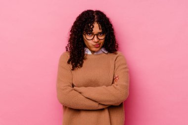 Pembe arka planda soyutlanmış, hoşnutsuzca kaşlarını çatan, kollarını kavuşturan genç melez bir kadın..