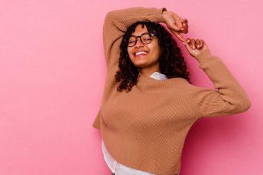 Pembe arka planda soyutlanmış genç melez bir kadın. Kollarını uzatıyor, rahat duruyor..