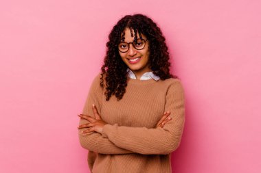 Pembe arka planda soyutlanmış genç melez bir kadın. Kendinden emin, kararlı kollarını kavuşturuyor..