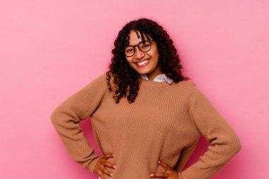 Pembe arka planda izole edilmiş genç melez kadın ellerini kalçasında tutuyor..