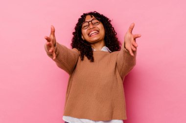 Pembe arka planda soyutlanmış genç melez bir kadın kameraya sarılıyor..