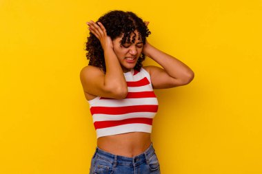 Sarı arka planda izole edilmiş, kulakları elleriyle kapatan genç bir ırk kadını..