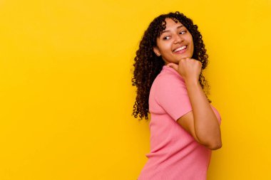 Sarı arka planda izole edilmiş genç melez bir kadın başparmak uzakta, gülüyor ve kaygısız..