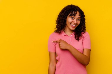 Sarı arka planda izole edilmiş genç melez kadın gülümsüyor ve boş alanda bir şeyler gösteriyor..