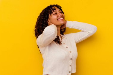 Sarı arka planda izole edilmiş genç melez bir kadın kendini güvende hissediyor, elleri başının arkasında..