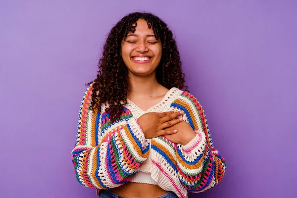 Mor arka planda soyutlanmış genç melez bir kadın. Gülüyor, ellerini kalbe koyuyor, mutluluk kavramını koruyor..