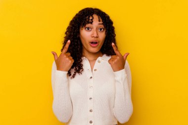 Sarı arka planda izole edilmiş, ağzı açık, üst tarafı gösteren genç melez bir kadın..