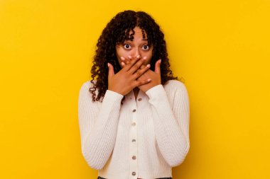 Sarı arka planda izole edilmiş genç bir ırk kadını elleriyle ağzını kapatırken şok oldu..