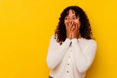 Sarı arka planda izole edilmiş genç bir ırk kadını bir şeye gülüyor, ağızlarını elleriyle kapatıyor..