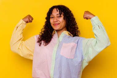 Sarı arka planda izole edilmiş genç bir ırk kadını güçlü bir jest yapıyor, kadınsı gücün sembolü.