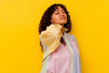 Genç melez kadın sarı arka planda izole edilmiş. Stres yüzünden boynu ağrıyor. Masaj yapıyor ve elle dokunuyor..
