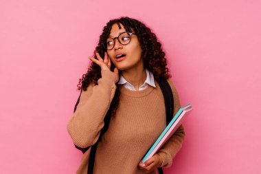 Genç öğrenci melez kadın pembe arka planda izole edilmiş bir şekilde bir dedikoduyu dinlemeye çalışıyor..
