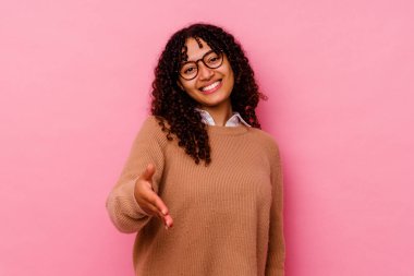 Pembe arka planda soyutlanmış genç melez bir kadın selamlaşma jesti olarak kameraya uzanıyor..