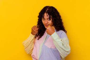 Sarı arka planda izole edilmiş genç bir ırk kadını bir tartışma yüzünden yumruk, öfke, kavga ve boks atıyor..